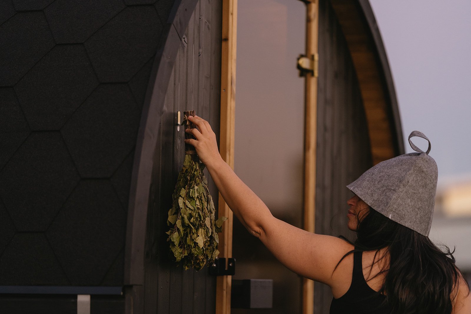 Woman wearing sauna hat with birch vihta at barrel sauna — sauna hat benefits