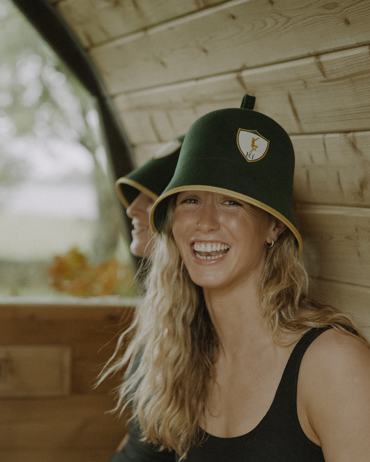 Athlete smiling to camera in the sauna wearing the Rí Sauna Crown, brim shading the eyes